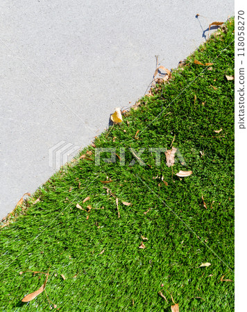 A close-up of artificial grass meeting a concrete sidewalk, scattered with a few fallen leaves. A close-up of artificial grass meeting a concrete sidewalk, scattered with a few fallen leaves. 118058270
