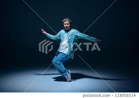 Stylish young guy, hip-hop dancer in motion on stage, training, performing with energy against navy blue background Stylish young guy, hip-hop dancer in motion on stage, training, performing with energy against navy blue background 118058514