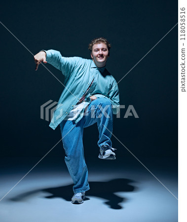 Artistic and joyful young man in casual clothes in motion on stage, performing hip hop against navy blue background Artistic and joyful young man in casual clothes in motion on stage, performing hip hop against navy blue background 118058516