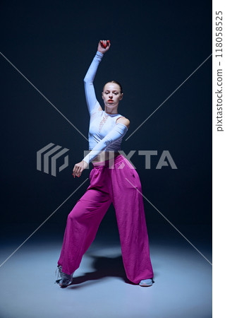 Full-length of emotional, beautiful, joyful young girl, hip hop dancer in motion, performing against navy blue background 118058525