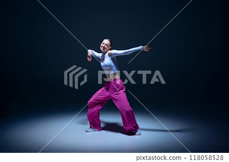 Powerful dance vibe. Young expressive girl in stylish outfit performing hip-hop against navy blue background. Passion and emotions. Powerful dance vibe. Young expressive girl in stylish outfit performing hip-hop against navy blue background. Passion and emotions. 118058528