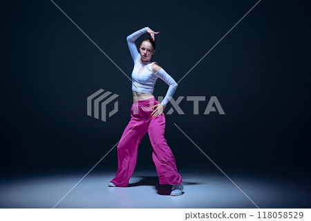 Powerful dance vibe. Young expressive girl in stylish outfit performing hip-hop against navy blue background. Artistic vibe. 118058529