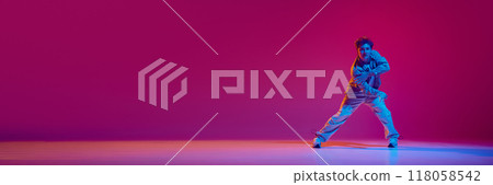 Energetic young man in casual clothes in motion, performing hip-hop dance against pink background in neon light 118058542