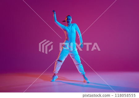 Talented and artistic young girl in white outfit dancing hip-hop with energy against pink background in neon light 118058555
