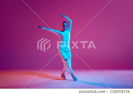 Talented and artistic young girl in white outfit dancing hip-hop with energy against pink background in neon light 118058556