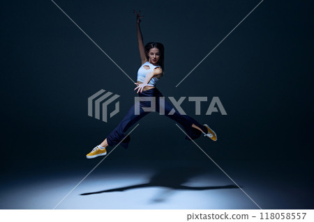 Dynamic image for young energetic girl, hip hop dancer in motion, performing with rhythm and style against navy blue studio background 118058557