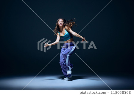 Dynamic image of young girl, dancer showing technique during focused hip hop training session against navy blue studio background 118058568