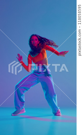 Burst of energy. Young girl in motion, dynamically dancing hip hop against gradient blue background in neon light 118058595