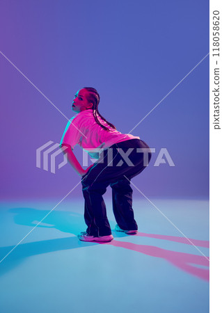 Catching beats. Stylish and artistic young girl, hip-hop dancer performing on stage with passion against gradient purple background in neon light Catching beats. Stylish and artistic young girl, hip-hop dancer performing on stage with passion against gradient purple background in neon light 118058620