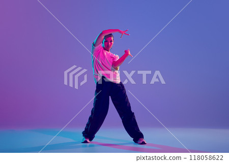 Dynamic image of artistic and expressive young girl, hip-hop dancer performing against gradient purple background in neon light 118058622