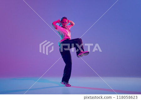 Dance school. Stylish and artistic young girl dancing hip hop with emotions against gradient purple background in neon light Dance school. Stylish and artistic young girl dancing hip hop with emotions against gradient purple background in neon light 118058623