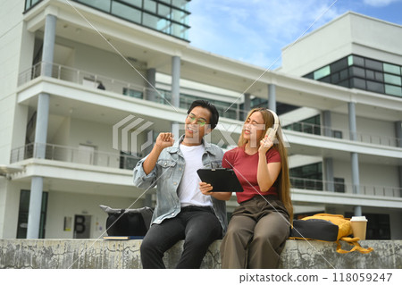 University student sitting on a ledge in front of building and talking to each other at break time University student sitting on a ledge in front of building and talking to each other at break time 118059247