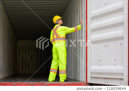 Male container logistic worker in yellow helmet and safety vest inspecting empty container before loading finish goods at cargo shipping yard.. 118059644
