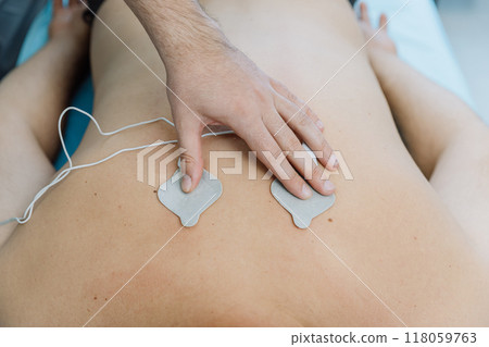 Electrotherapy session with electrodes for back pain relief in a physiotherapy clinic setting 118059763