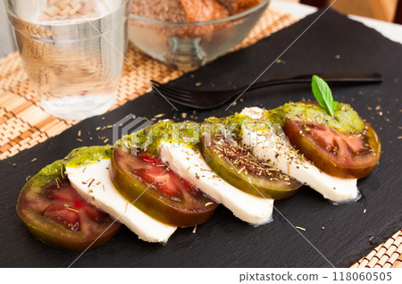 Caprese salad with mozzarella, black tomatoes and pesto on black stone plate Caprese salad with mozzarella, black tomatoes and pesto on black stone plate 118060505