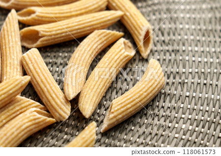Uncooked organic penne quinoa pasta on a textured braided rustic cloth. Unique raw natural ingredients for gluten free diet  118061573
