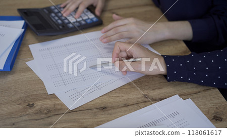 Accountants or auditors reviewing financial documents while sitting at the wooden desk in office. Professionals analyzing paper reports and using calculators, close up. Audit and taxes concept Accountants or auditors reviewing financial documents while sitting at the wooden desk in office. Professionals analyzing paper reports and using calculators, close up. Audit and taxes concept 118061617