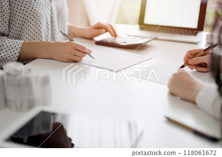 Two accountants using a calculator and laptop computer for counting taxes or revenue balance while rolls of receipts are waiting to be calculating. Business audit and taxes concepts 118061672