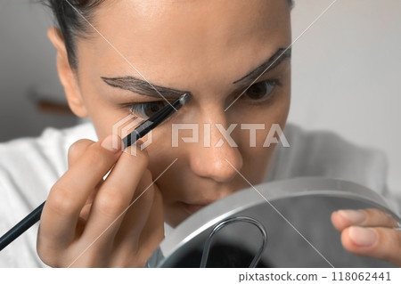 Woman applying paint on eyebrows making beauty procedure at home, closeup view. Woman applying paint on eyebrows making beauty procedure at home, closeup view. 118062441