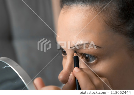 Young woman is painting contour of eyebrows using pencil before painting them. 118062444