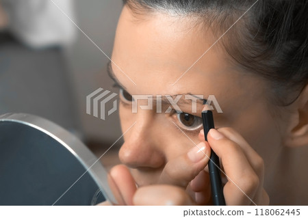 Young woman is painting contour of eyebrows using pencil before painting them. 118062445