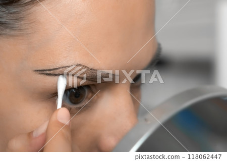 Young woman erases contour line around eyebrows with a cotton swab, closeup. 118062447