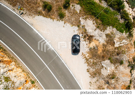 Top view of black car with a roof box, parked on a wide cliffside road. 118062903