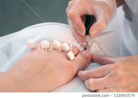Pedicurist master is applying base coal for shellac on woman's nails on toes. Pedicurist master is applying base coal for shellac on woman's nails on toes. 118063579