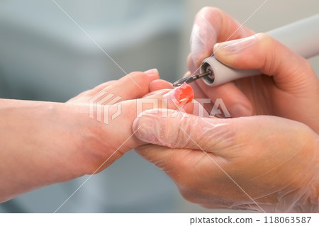 Pedicurist woman removes shellac polish from toes using manicure machine. 118063587