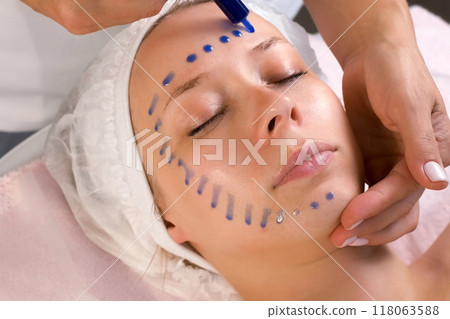 Cosmetologist is applying blue moisturizing serum on woman's face in beauty clinic. Cosmetologist is applying blue moisturizing serum on woman's face in beauty clinic. 118063588