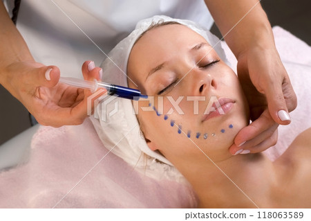 Cosmetologist is applying blue moisturizing serum on woman's face in beauty clinic. 118063589