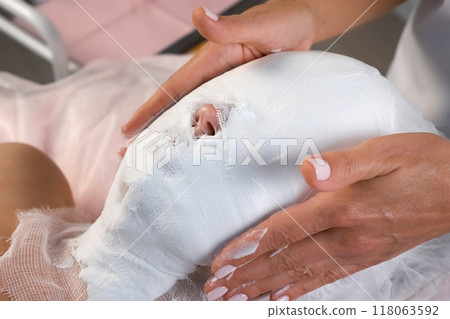Professional cosmetologist is covering woman's face with foam mask and gauze. Professional cosmetologist is covering woman's face with foam mask and gauze. 118063592