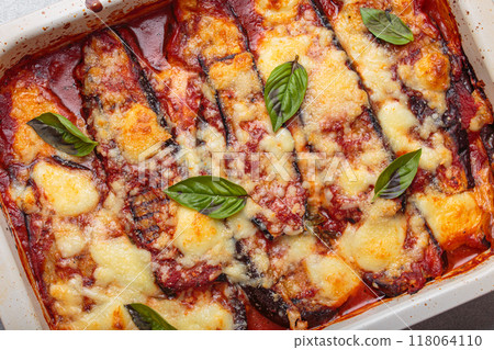 Eggplant parmigiana di melanzane with tomato sauce and basil leaves baking in a white ceramic dish, close up top view 118064110