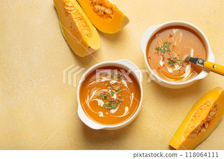 Two bowls of creamy pumpkin soup decorated with parsley and pepper on warm yellow beige background top view 118064111