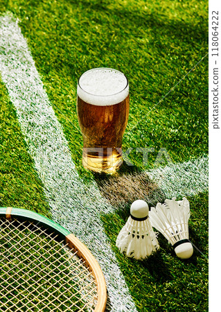 Refreshing beer meets badminton on field. Racket, shuttlecocks, and cold drink come together, highlighting fun of outdoor sports and relaxation. 118064222