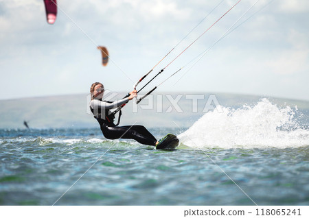CLOSE UP, Fit Caucasian tourist kiteboarding along peninsula. Relaxed young woman surfing boarding and exploring Mediterranean coastline on sunny summer day 118065241