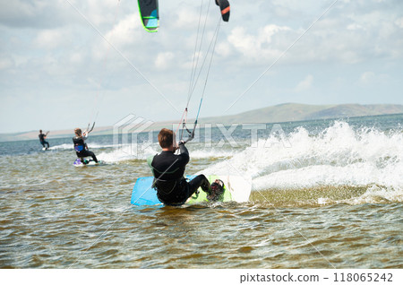 Kitesurfing, kiteboarding, action photo. Man from behind actively and quickly rides on water on kiteboard, sailing, adrenaline Kitesurfing, kiteboarding, action photo. Man from behind actively and quickly rides on water on kiteboard, sailing, adrenaline 118065242