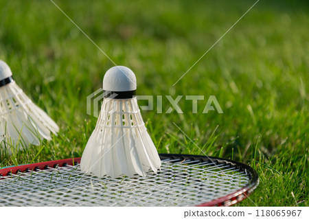 White badminton shuttlecock and badminton rackets on green grass in sunny shadow. Summer. Leisure games. Outdoors. Close up. White badminton shuttlecock and badminton rackets on green grass in sunny shadow. Summer. Leisure games. Outdoors. Close up. 118065967