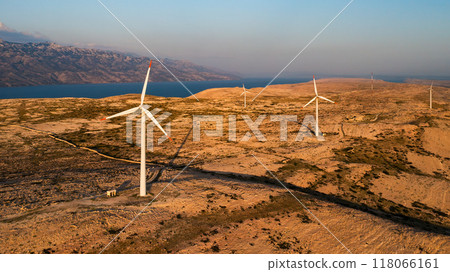 PAG ISLAND, CROATIA - JULY 14 2024: Wind turbines mounted near sea water on Pag Island. Coastline provides excellent conditions for wind energy due to strong winds in Croatia 118066161