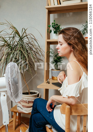 fan cools unhappy Caucasian woman languishing in summer heat. warmed-up experiences hot flashes fan cools unhappy Caucasian woman languishing in summer heat. warmed-up experiences hot flashes 118066184