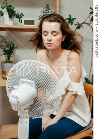 fan cools unhappy Caucasian woman languishing in summer heat. warmed-up experiences hot flashes 118066185
