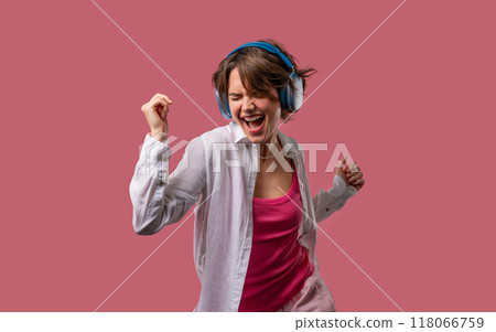 Young woman listening streaming music, enjoying dance with headphones on pink Young woman listening streaming music, enjoying dance with headphones on pink 118066759