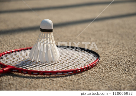 White badminton feather shuttlecock and badminton racket on beige floor sport badminton court in sunny shadow. Summer game outdoors. Close up. 118066952