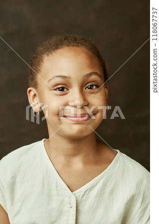 Vertical portrait of young smiling African American girl looking at camera posing on brown background at studio 118067737