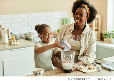 Laughing African American young mother and little daughter enjoying quality time while cooking together making fruit smoothie in blender at beige kitchen, copy space Laughing African American young mother and little daughter enjoying quality time while cooking together making fruit smoothie in blender at beige kitchen, copy space 118067827