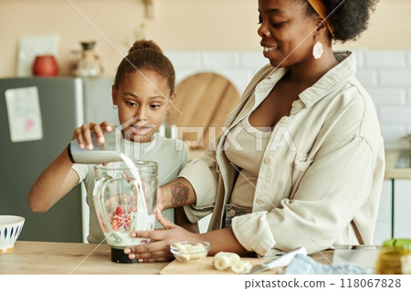 Cute African American girl making smoothie carefully adding milk to blender while Cute African American girl making smoothie carefully adding milk to blender while 118067828