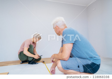 Father and adult son installing flooring in new Home by their own. Doing measurements, calculating for vinyl laminate and skirting. DIY, Do it yourself. Home renovation, improvement, refurbishment Father and adult son installing flooring in new Home by their own. Doing measurements, calculating for vinyl laminate and skirting. DIY, Do it yourself. Home renovation, improvement, refurbishment 118068108