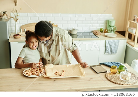 High angle shot of African American loving grandmother hugging with adoration laughing girl while baking homemade cookies together at wooden kitchen counter, copy space High angle shot of African American loving grandmother hugging with adoration laughing girl while baking homemade cookies together at wooden kitchen counter, copy space 118068160