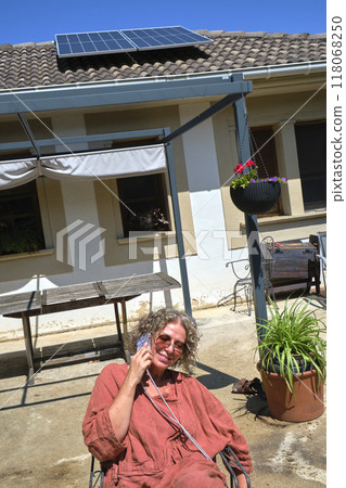 Woman talking on the phone while sitting in a sunny backyard Woman talking on the phone while sitting in a sunny backyard 118068250