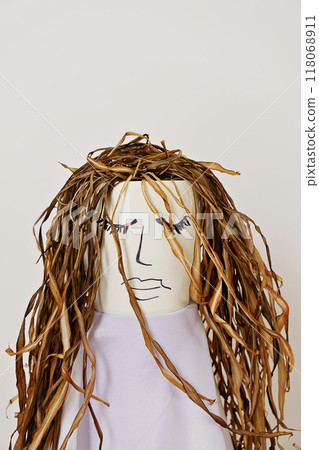 Ceramic pot featuring a hand-drawn face and dried plant leaves hair stands against simple neutral background 118068911